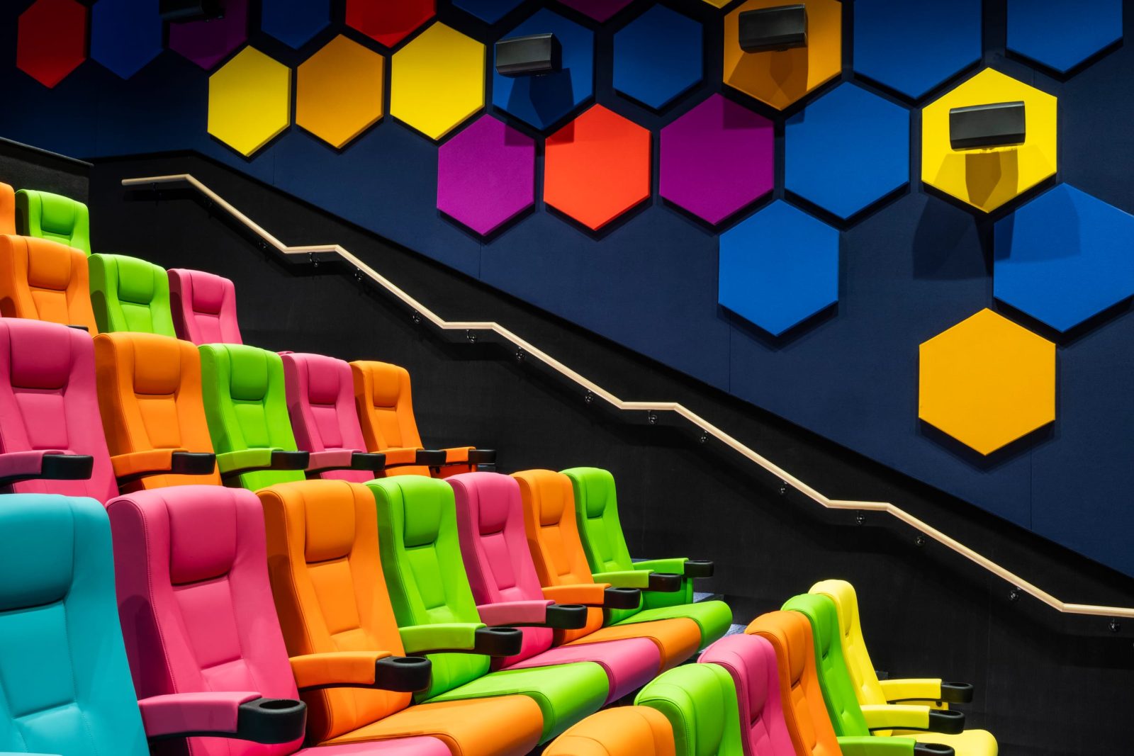 Tiered seating beside the stepped handrail, beneath hexagonal acoustic wall panels